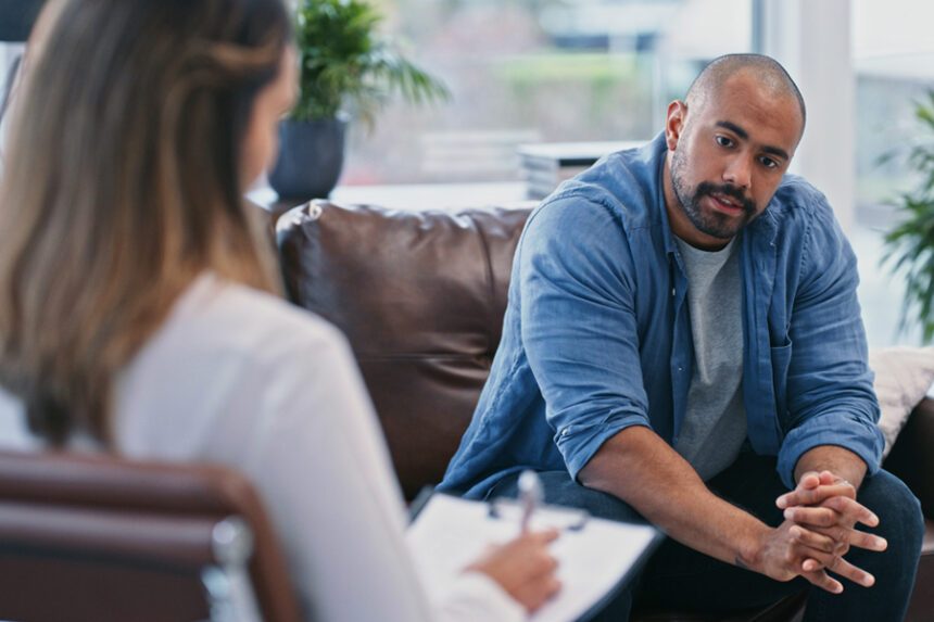 Man sits on couch talking while a therapist sits in a chair, taking notes