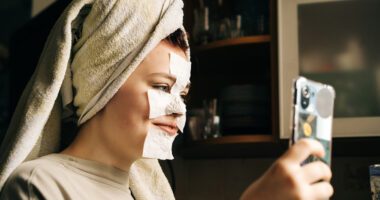 teenage with with skin-care face mask on her face takes a selfie with her phone