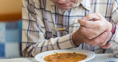 Old man uses both hands to hold a spoonful of soup