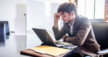 Man in work suit looks at laptop, frustrated