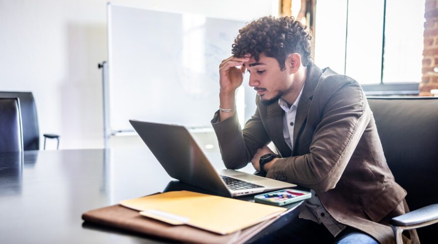 Man in work suit looks at laptop, frustrated