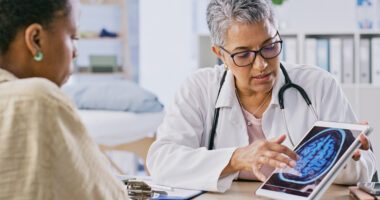 A doctor shows a patient a brain scan image on a tablet while explaining the results during a medical consultation