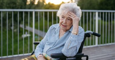 Adult woman sitting in a wheelchair with her hand on her head
