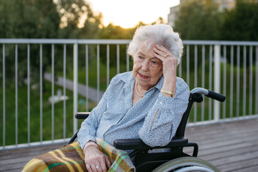 Adult woman sitting in a wheelchair with her hand on her head