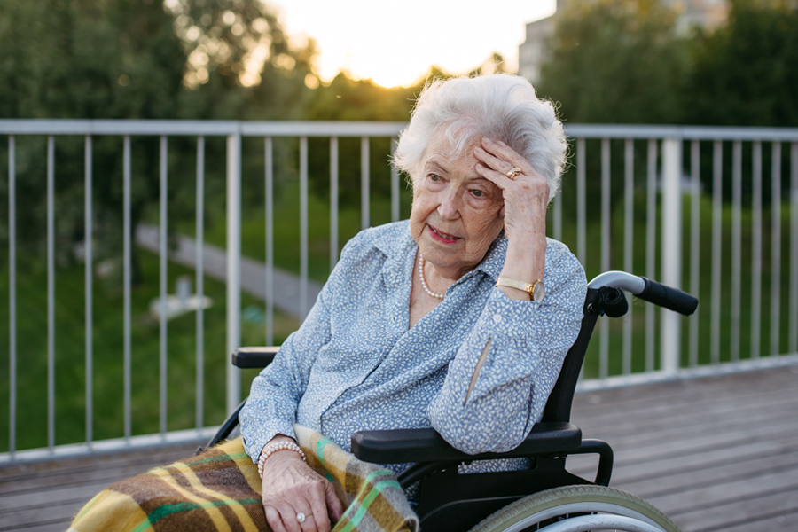 Adult woman sitting in a wheelchair with her hand on her head