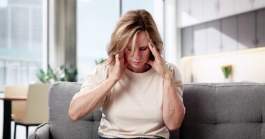 Woman sitting with her hands on her temples, showing signs of pain or dizziness.