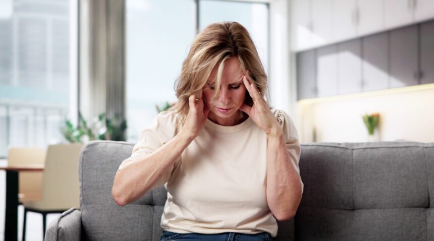 Woman sitting with her hands on her temples, showing signs of pain or dizziness.