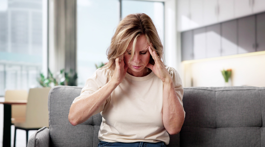 Woman sitting with her hands on her temples, showing signs of pain or dizziness.