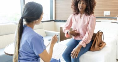 women sits on exam table dressed in normal clothes, talking to female provider