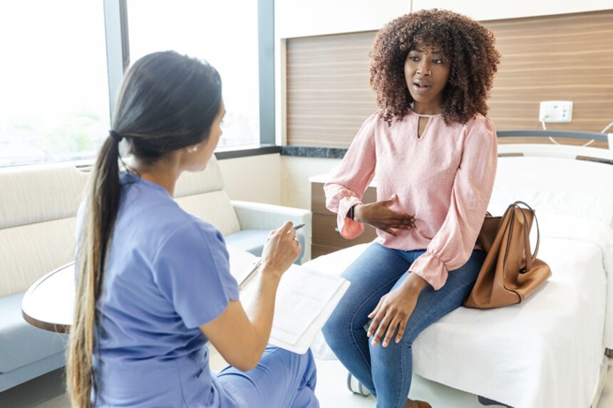 women sits on exam table dressed in normal clothes, talking to female provider