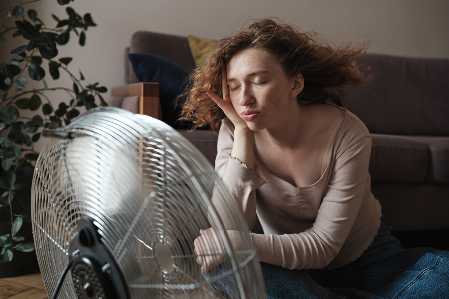 young woman sits in front of a metal cooling fan, eyes closed.