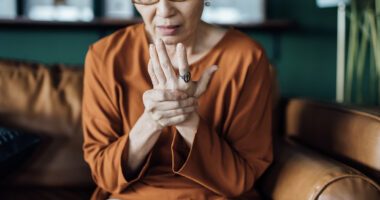 Woman sitting on a couch holding her hand with a pained expression, possibly due to joint discomfort.