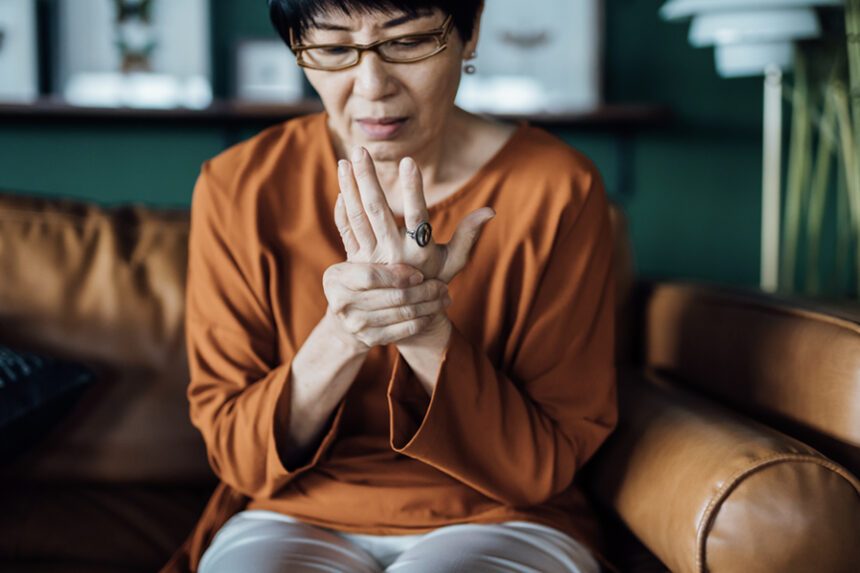 Woman sitting on a couch holding her hand with a pained expression, possibly due to joint discomfort.
