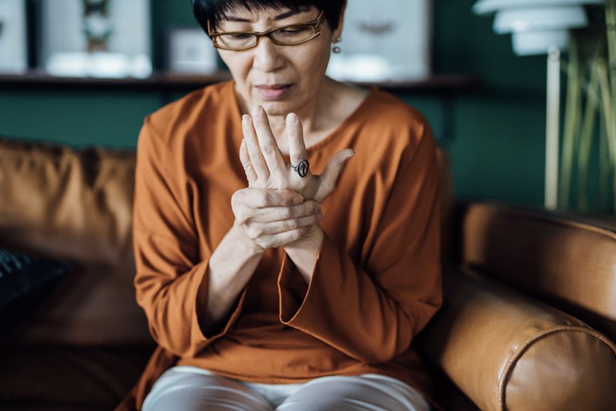 Woman sitting on a couch holding her hand with a pained expression, possibly due to joint discomfort.