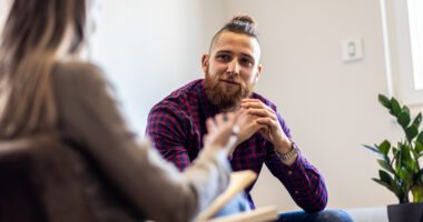 Trendy young man talks to a therapist, sitting in adjacent chairs