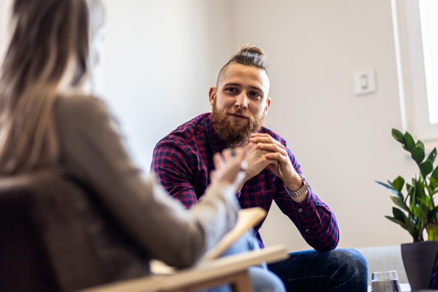Trendy young man talks to a therapist, sitting in adjacent chairs