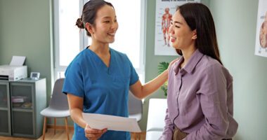 A healthcare professional is having a friendly conversation with a patient during a medical consultation in a clinical setting.