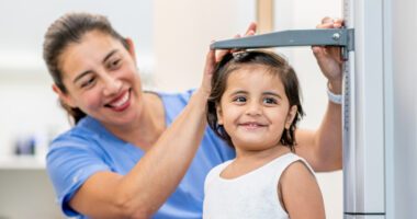 A smiling nurse measures a young girl’s height during a medical checkup.