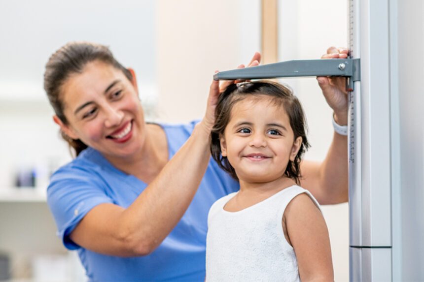 A smiling nurse measures a young girl’s height during a medical checkup.