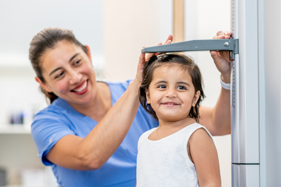 A smiling nurse measures a young girl’s height during a medical checkup.