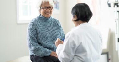 An older woman smiles while talking with her doctor during a checkup.