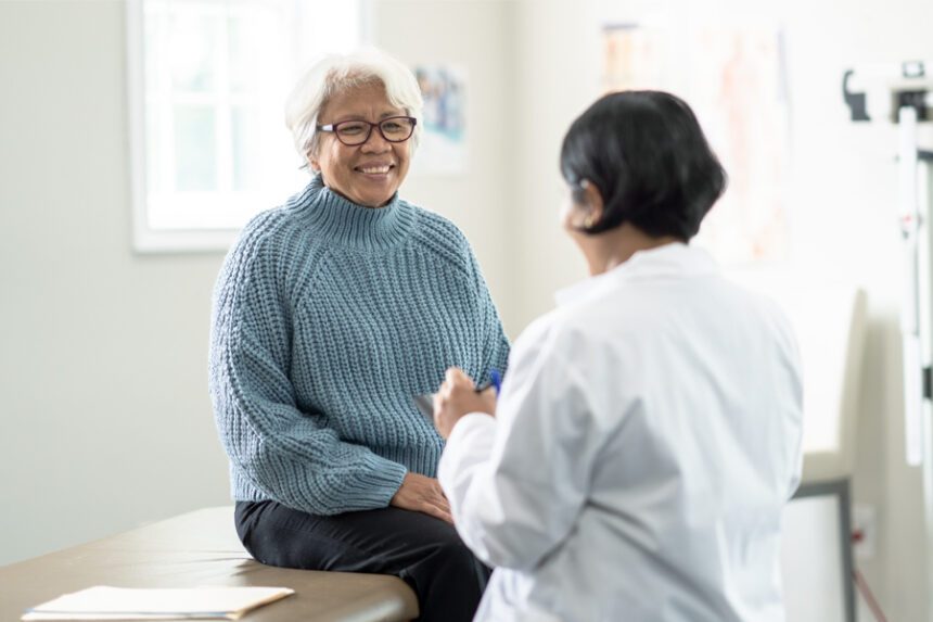 An older woman smiles while talking with her doctor during a checkup.
