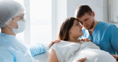 A pregnant woman receives support from a doctor and her partner during labor in a hospital.