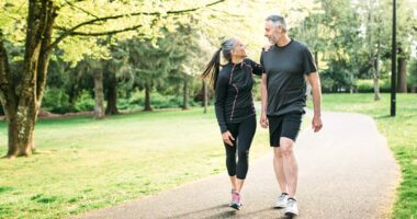 Couple in their 50's walk in a park, wearing fitness clothes