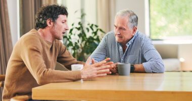 Adult son talks to his elderly father at the kitchen table