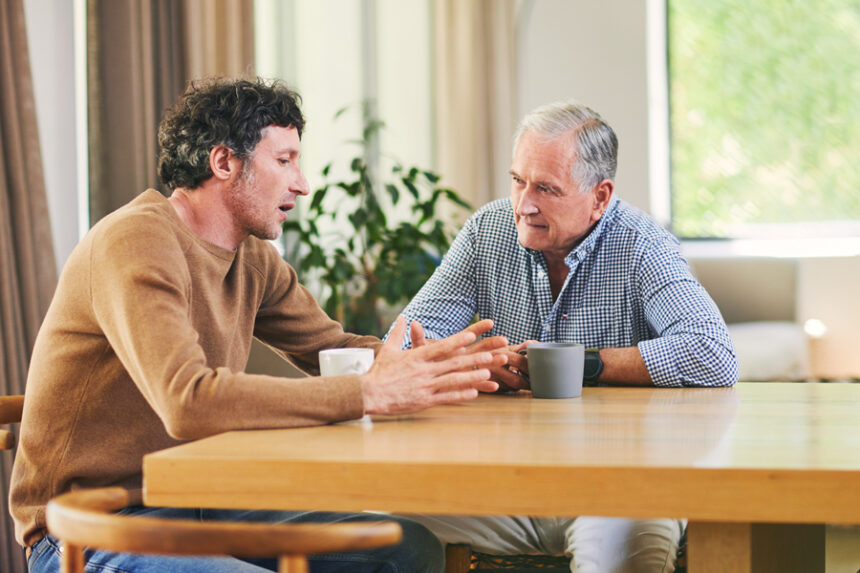 Adult son talks to his elderly father at the kitchen table
