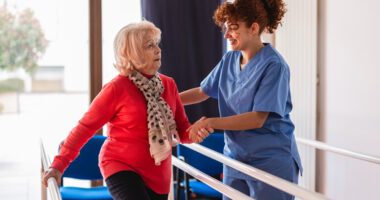 Older woman assisted by a healthcare professional during rehab exercises.