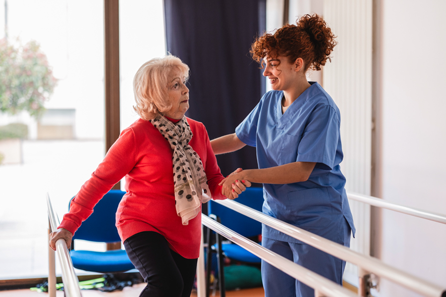 Older woman assisted by a healthcare professional during rehab exercises.