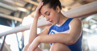 teenaged female athlete rests next to a balance beam