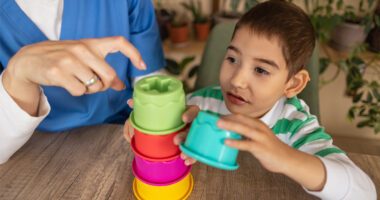 A child is stacking colorful cups while an occupational therapist guides him with instructions.