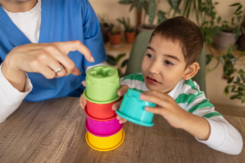 A child is stacking colorful cups while an occupational therapist guides him with instructions.