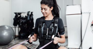 A woman works out with resistance bands while wearing a weighted training vest.
