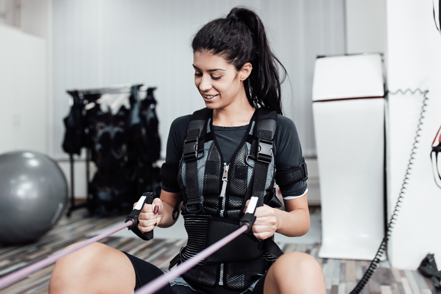 A woman works out with resistance bands while wearing a weighted training vest.