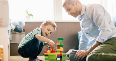 ChatGPT said: An adult man and a young boy build a colorful block tower together on the floor, enjoying a moment of play and learning at home.