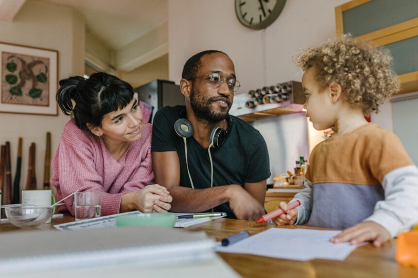 ChatGPT said: A family shares a moment at the table as the parents listen to and support their young child while they draw.