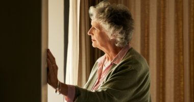 Elderly woman gazing out the window, lost in thought.