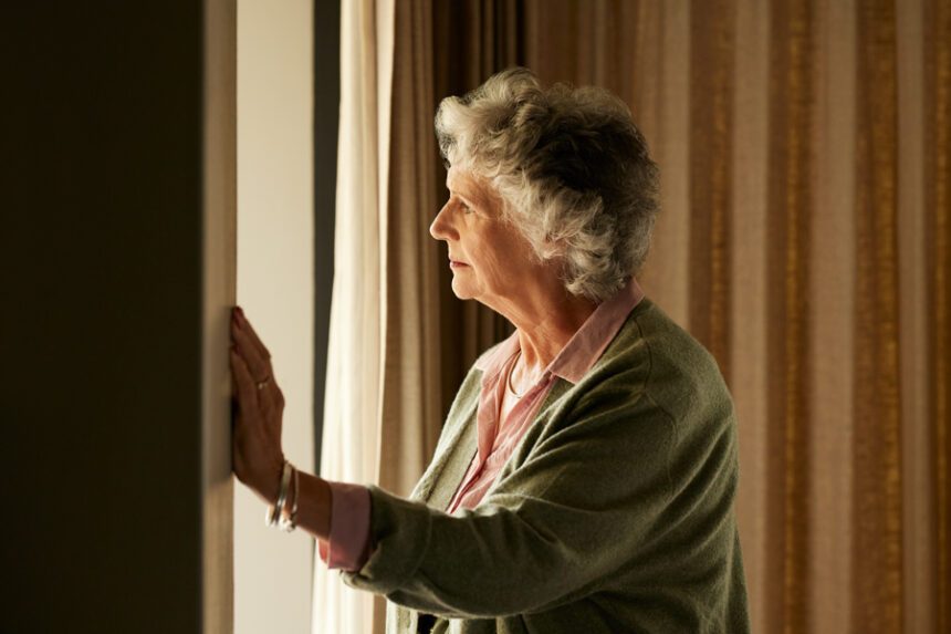 Elderly woman gazing out the window, lost in thought.