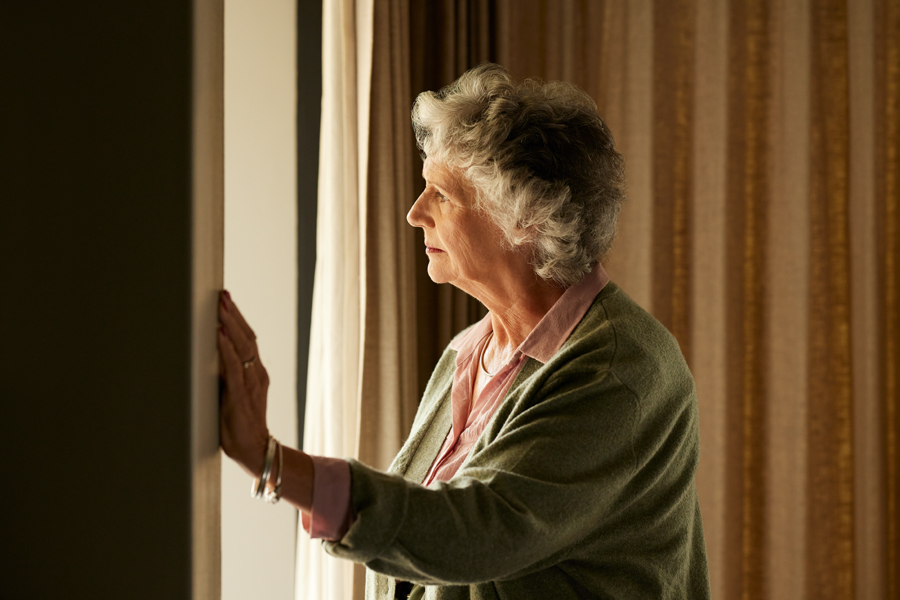 Elderly woman gazing out the window, lost in thought.