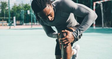 A man holds his knee in pain while exercising outdoors.