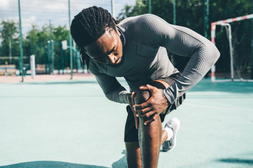 A man holds his knee in pain while exercising outdoors.