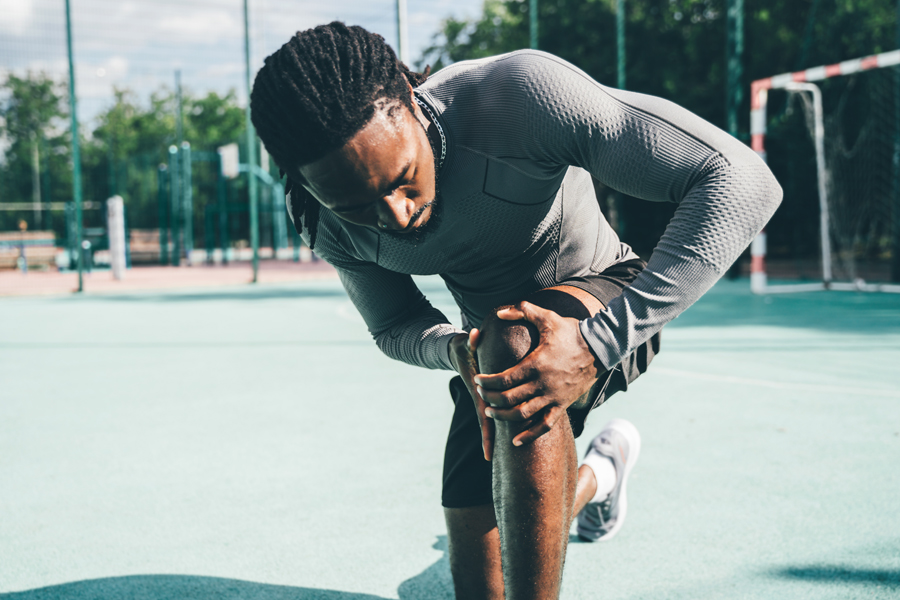A man holds his knee in pain while exercising outdoors.