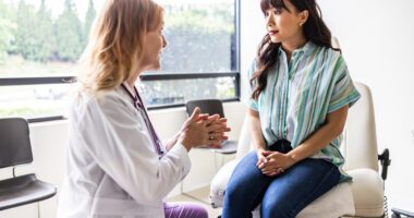 A healthcare provider is talking with a patient who is sitting on the exam table during a medical consultation.