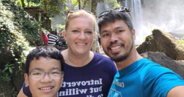 Jenn and Damson Huon smile with their son, Bohao, during a family outing by a waterfall.