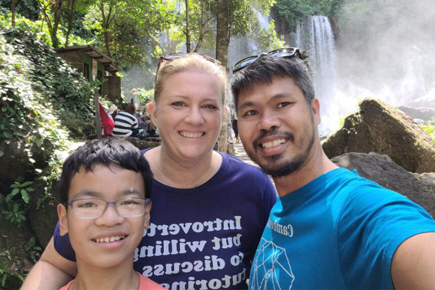 Jenn and Damson Huon smile with their son, Bohao, during a family outing by a waterfall.