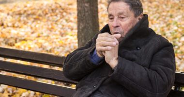 Man sits on bench, warming hands with breath