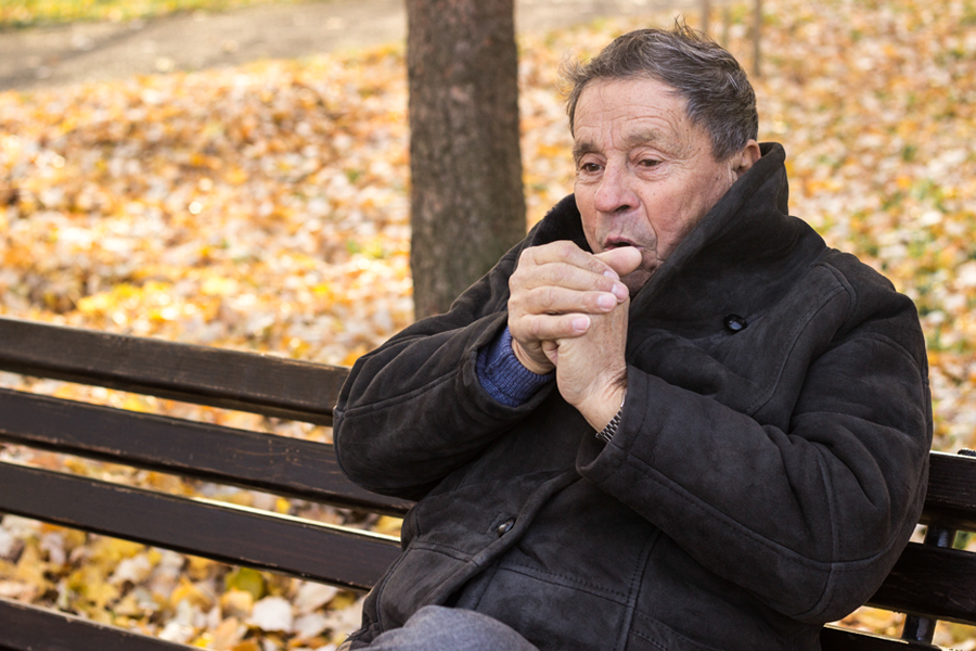 Man sits on bench, warming hands with breath
